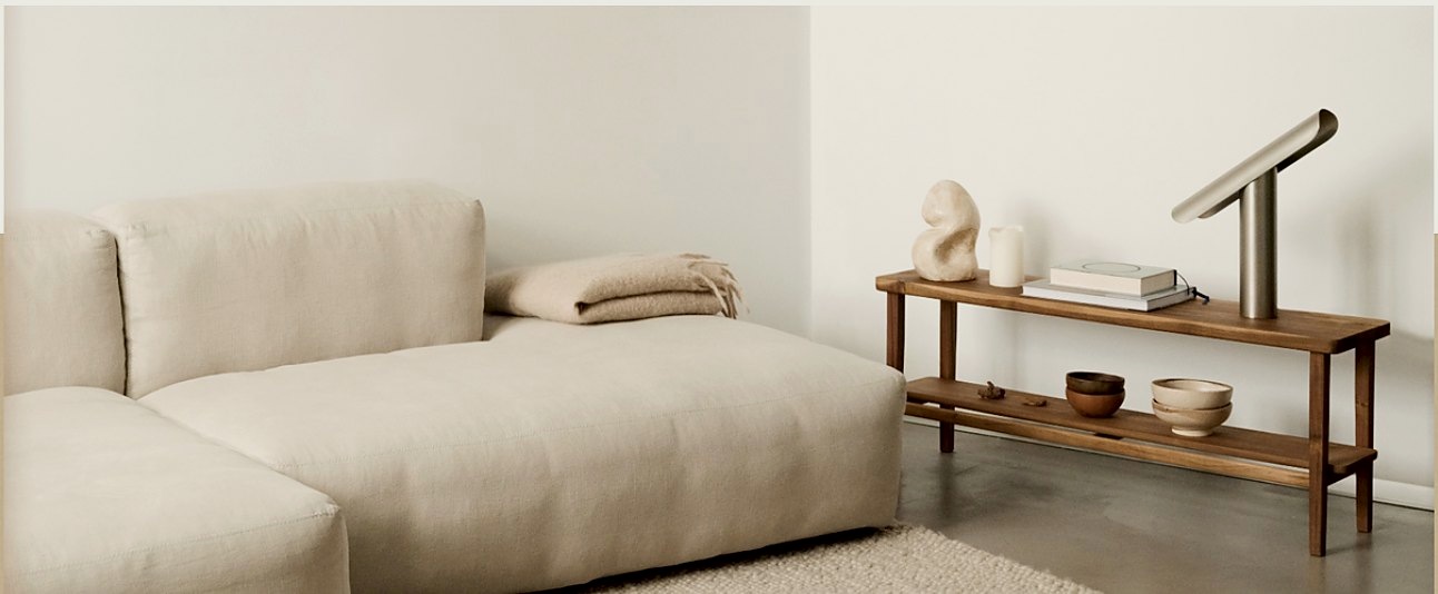A calm, sunlit living room with a linen sofa and a wooden console table.
